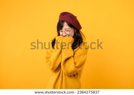 Shy and joyful. A young woman, wearing a yellow sweater, red beret, and eyeglasses, shares a moment of surprise against a vibrant yellow background.