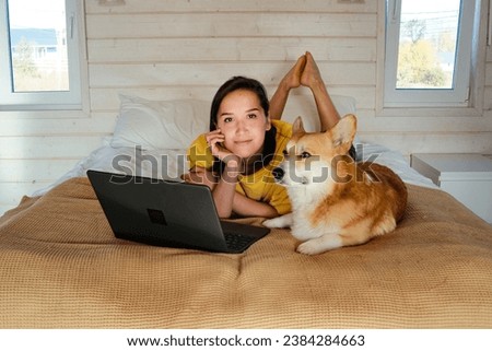 Young woman works from home on laptop, smiles with pet corgi dog. High quality photo