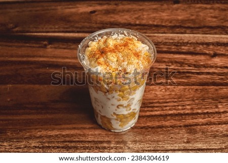 Elote en Vaso - Mexican Street Corn in a Cup - a clear cup featuring mayo, corn, cortina, lime and chili powder on a dark table Royalty-Free Stock Photo #2384304619