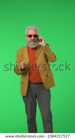 Portrait senior stylish hipster on Chroma key green screen background, man looks at camera talking on smartphone. Advertising area, workspace mockup. Vertical photo. Royalty-Free Stock Photo #2384317517