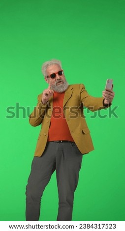 Portrait senior stylish hipster on Chroma key green screen background, elegant man posing for selfie on smartphone. Advertising area, workspace mockup. Vertical photo.