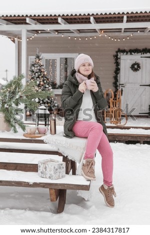 A woman in winter clothes with a hot drink in the courtyard of a house decorated for Christmas.