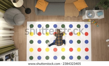 Top view of the bright room, twister game laying on the floor, kid playing, stepping on colorful areas with hands and legs. Royalty-Free Stock Photo #2384323405