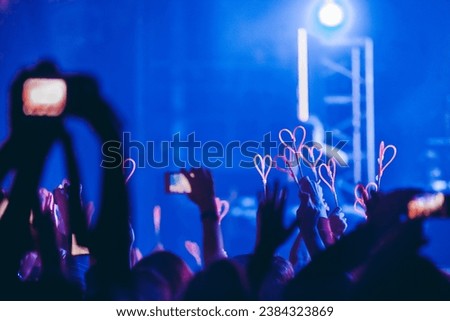 Concert fans' hands holding glowing neon sticks and smartphones during the concert. Royalty-Free Stock Photo #2384323869