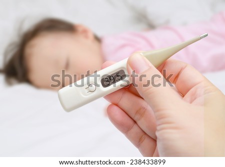 Mother holding thermometer foreground and sick little girl in bed