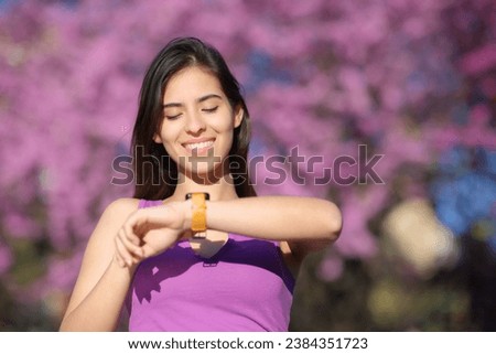 Front view portrait of a happy woman checking smartwatch in a violet park