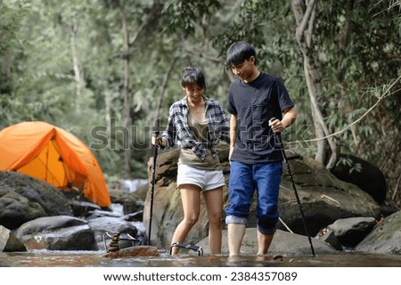 Asian Teenagers walk in the natural stream with a camping tent in the background, Enjoying the relaxing atmosphere of the surrounding nature.