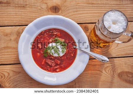 Close up picture on the vintage style deep plate with traditional borsch soup and mug of pilsner lager beer served on the rustic wooden table. Healthy and satisfying dish from eastern european cuisine