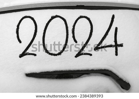 Drawing 2024 on the windshield of a car covered in snow
