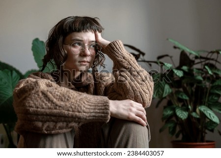 Lonely stressed teenager sitting at home alone looking at window, thinking of life, problems, misunderstanding with friends, parents. Depressed teen in puberty crisis with absence of life motivation Royalty-Free Stock Photo #2384403057