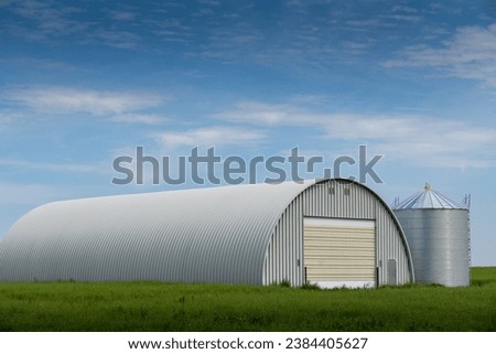 Farmyard quonset used for storing agriculture machinery overlooking a grain silo on the Canadian prairies in Kneehill Country Alberta Canada.