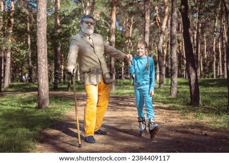 Grandfather walks with his granddaughter in the park. A girl roller skates in the park with her old grandfather. A funny grandfather and a little girl are playing and joking.