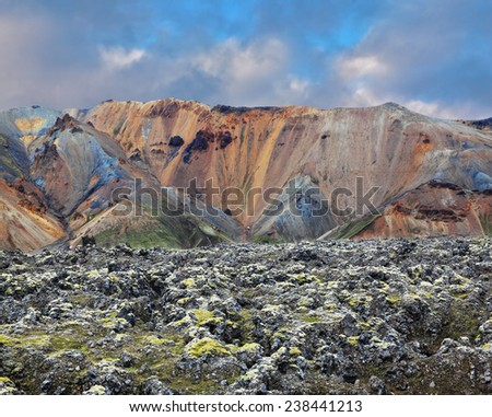 National Park Landmannalaugar in Iceland. Pieces of gray and black lava, sometimes covered with green moss. In the background -  orange and blue rhyolite mountains