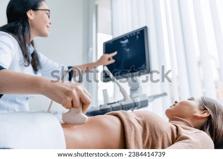 Mid adult female doctor using ultrasound scanner. Fertility pregnancy ovulation concept. Gynecologist telling and showing patient embryo. Prenatal period Royalty-Free Stock Photo #2384414739