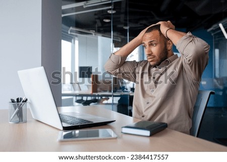 Frustrated and sad man at workplace reading online message from laptop, businessman sitting inside office at workplace, desperate unhappy, got bad news, bankruptcy, layoff. Royalty-Free Stock Photo #2384417557