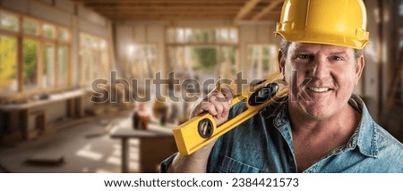 Happy Male Contractor at a Construction Site Wearing a Hard Hat and Work Gloves Holding His Level. Royalty-Free Stock Photo #2384421573
