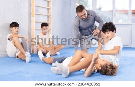 Focused adolescent boys engaging in self-defense course, working on kimura maneuver in training bout under careful supervision of experienced trainer Royalty-Free Stock Photo #2384428061