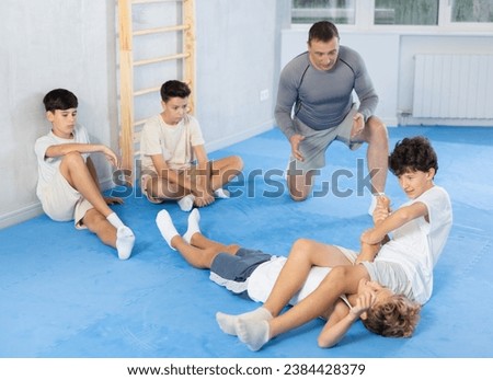 Teenage boys practicing armbar technique in simulated sparring session at gym during self-defense training under watchful eye of instructor Royalty-Free Stock Photo #2384428379