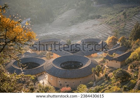 The Fujian tulou, old traditional rural dwellings in China aerial view. Buildings behind the golden trees, sunset picture, terraces at the background