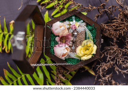 A pair of engagement rings in a wooden glass box decorated with pink and yellow flowers, on a blurred background. An engagement ring is a symbol of love and commitment. Selective focus.