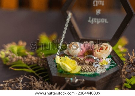 A pair of engagement rings in a wooden glass box decorated with pink and yellow flowers, on a blurred background. An engagement ring is a symbol of love and commitment. Selective focus.