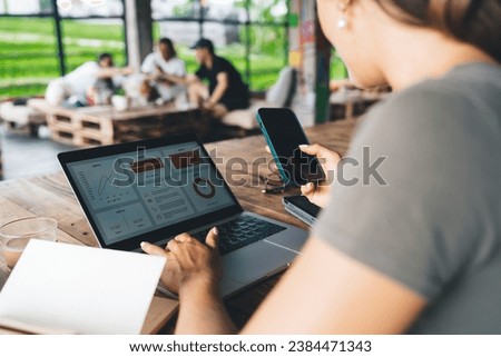 Unrecognizable woman checking smartphone during work on laptop