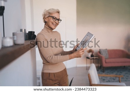 Cheerful senior woman holding photo frame in living room