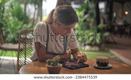 Woman draw land scape cowork cafe. Digital designer paint art pic. Illustrator work tablet pad. Artist use stylus pen outside. Girl develop job skill. Ipad sketch app. Coffee cup outdoor US. Hold mug.