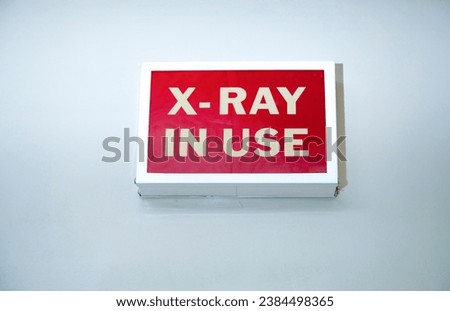 Vintage box shaped sign on a wall stating X-Ray In Use with white letters on a red background