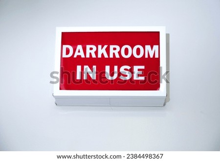 Vintage box shaped sign on a wall stating Darkroom In Use with white letters on a red background