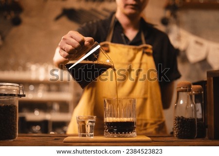 A female barista is pouring an americano or filter coffee to a glass. Concept of vintage cafe or coffee shop. Close up of hand pour black coffee ready to serve. Preparation, aroma and smoke.
