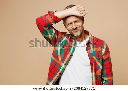 Adult tired sick ill sad man wear red shirt white t-shirt casual clothes hand on forehead suffer from headache isolated on plain pastel light beige color background studio portrait. Lifestyle concept