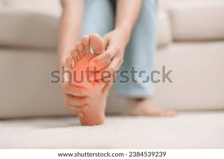 woman having barefoot pain during sitting on couch at home. Foot ache due to Plantar fasciitis and waking longtime. Health and medical concept Royalty-Free Stock Photo #2384539239