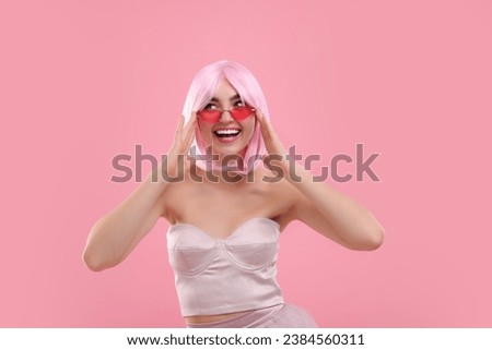 Pink look. Beautiful girl in wig and clothes wearing bright sunglasses on color background