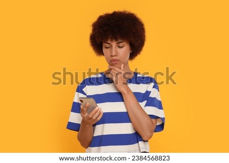 Thoughtful young woman with smartphone on orange background