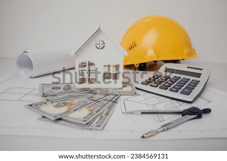 Construction drawings with helmet, calculator and model of house, cost of building.