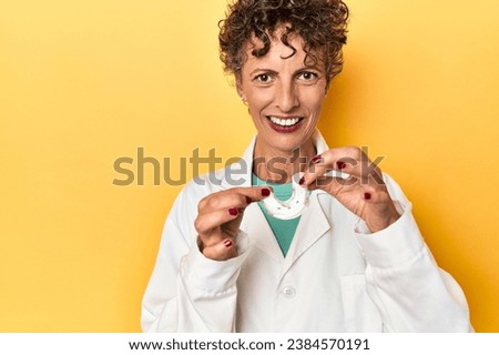 Dental doctor presenting invisible teeth aligner on yellow studio backdrop