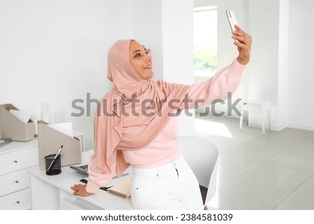 Mature Muslim woman with mobile phone taking selfie at home