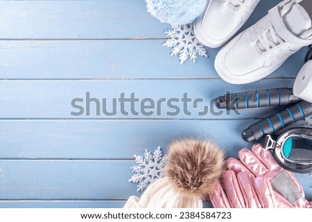 Winter sport and fitness, active lifestyle background. Warm knitted hat, sweater, jump rope, ski mask, thermal mug with hot tea, gloves, winter sneakers on wooden blue background, snowflakes, top view