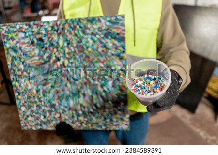 A close-up shot of a painting made from shredded recycled plastic caps placed in a glass next to her