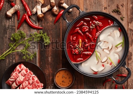 Overhead shot of Chinese Sichuan two-flavor hot pot, spicy and mushroom soup. Top view. Royalty-Free Stock Photo #2384594125