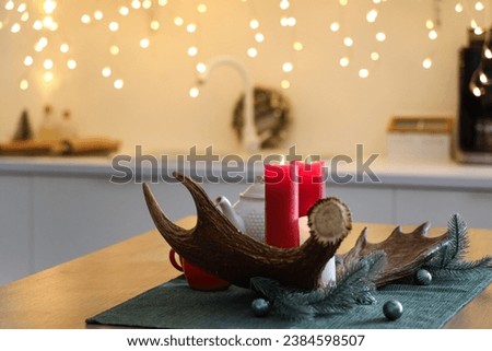 Moose antler with burning candles and Christmas branches on table in kitchen, closeup