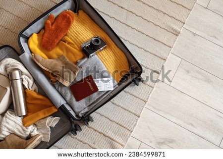 Open suitcase with travelling accessories and winter clothes on carpet, top view Royalty-Free Stock Photo #2384599871