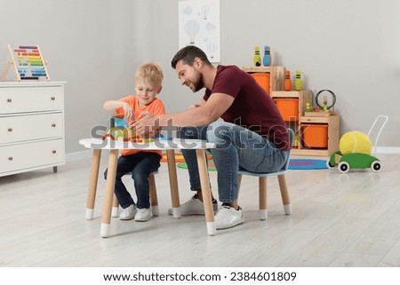Motor skills development. Happy father helping his son to play with colorful wooden arcs at white table in room Royalty-Free Stock Photo #2384601809