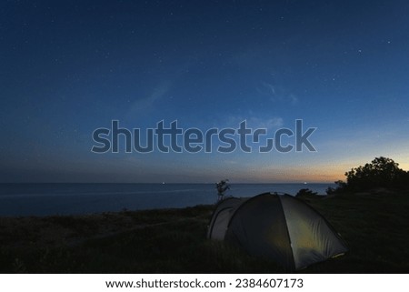 Wild camping in nature with a tent near the sea cliff at night under the starry sky. High quality photo