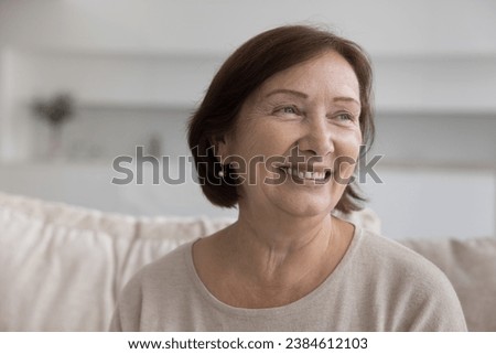 Head shot close up portrait happy dreamy senior woman daydreaming, sitting on couch at home, laughing staring into distance, enjoying carefree time on retirement, medical insurance cover for olders Royalty-Free Stock Photo #2384612103