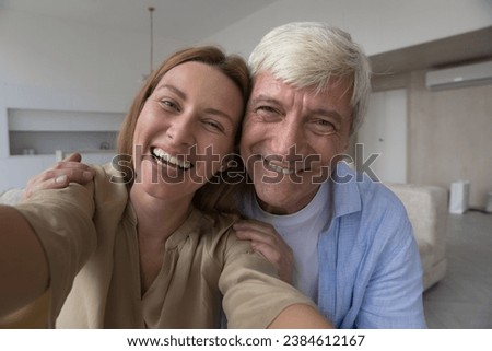 Laughing pretty woman and grey-haired father take selfie picture using device, make videocall talk to friend, having fun, record videos staring at camera, close up webcam faces view. Family portrait