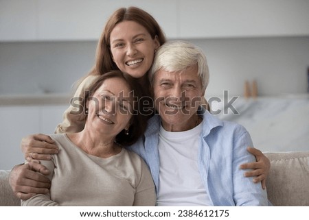 Portrait of young adult caring daughter with mature attractive parents smiling look at camera. Happy multi-generational family enjoy their warm, good, harmonic relationships, showing unity and support Royalty-Free Stock Photo #2384612175