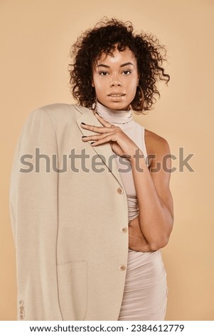 fashionable african american woman posing in autumn blazer and mini dress on beige background