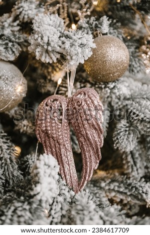 Golden ball, pink angel wings and shiny Christmas decorations and glittering toys on tree. Fir tree decorated with garlands. Happy New Year and Merry Christmas. Decor and interior decoration. Closeup.